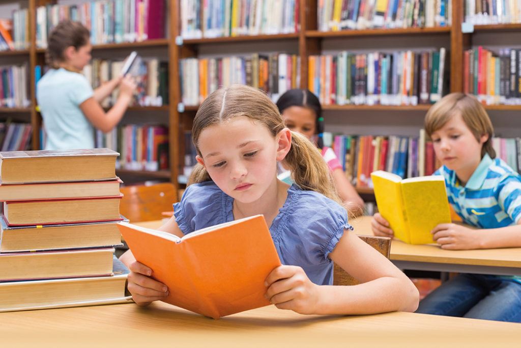 Close up of girl and others reading books in a library